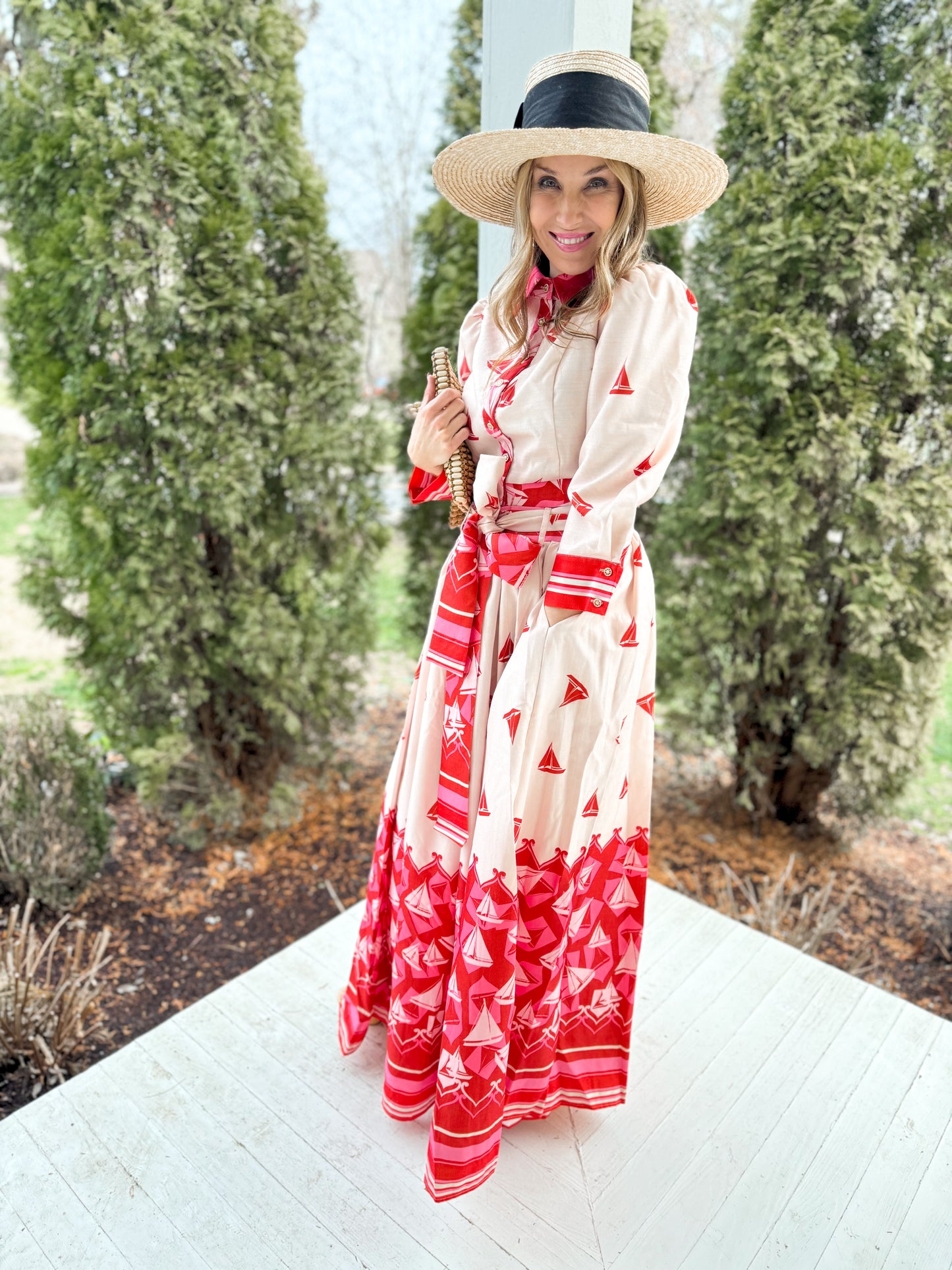 full side view woman standing on a porch wearing a cream and red sailbost blouse with 3/4 sleeves and a matching skirt with a tie around waist