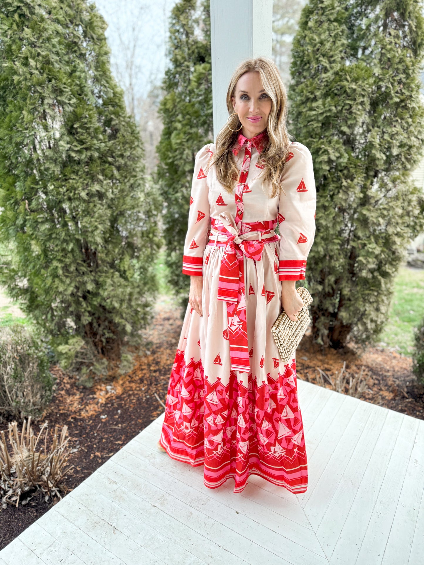 full front view woman standing on a porch wearing a cream and red sailbost blouse with 3/4 sleeves and a matching maxi skirt with a tie around waist