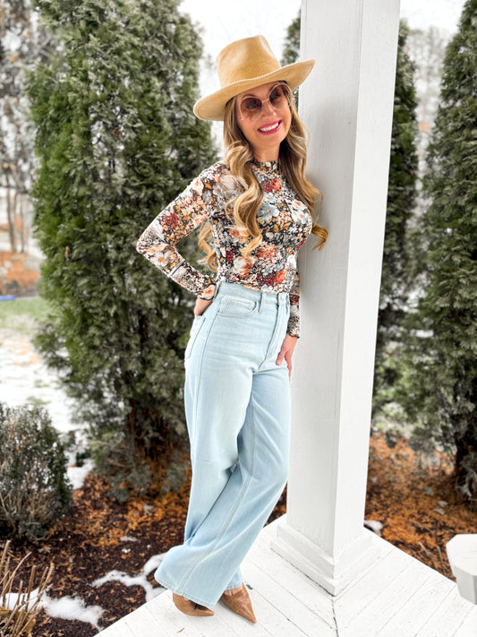 woman wearing light wash  high waisted retro straight denim jeans with a floral mesh top and tan hat and heels on the porch