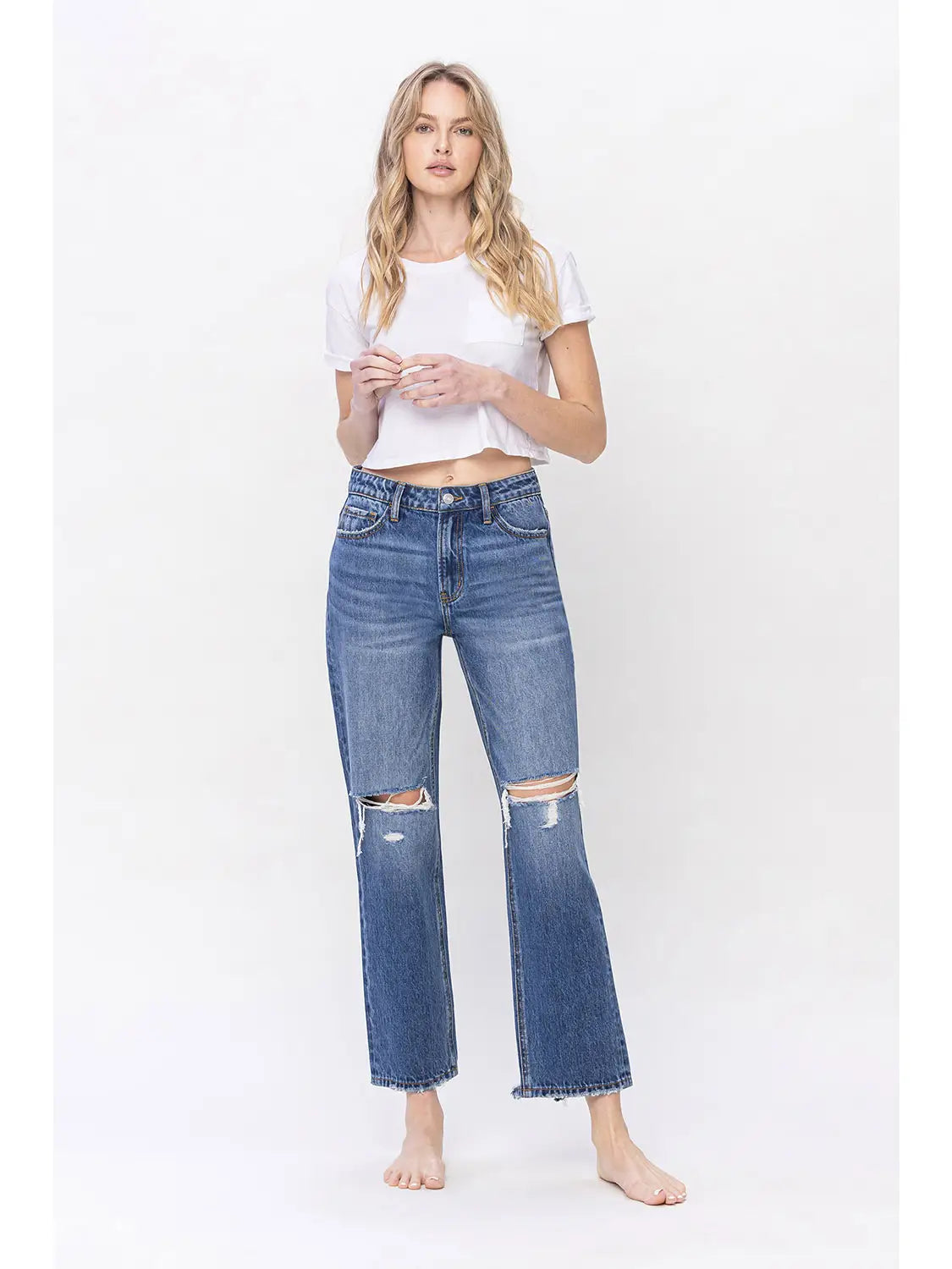 woman wearing high rise straight leg distressed knee denim jeans with white crop top in front of a white background